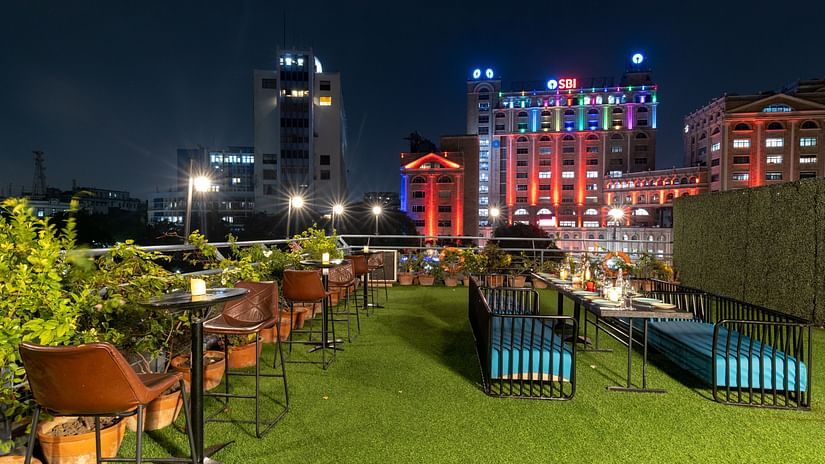 A nighttime view of a rooftop dining area with a green grass floor and a table set for a meal, city lights in the distance.