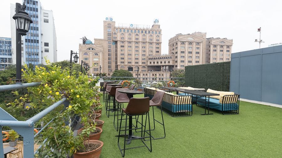 A rooftop garden cafe with artificial grass, potted plants, and a view of an ornate building in the background.