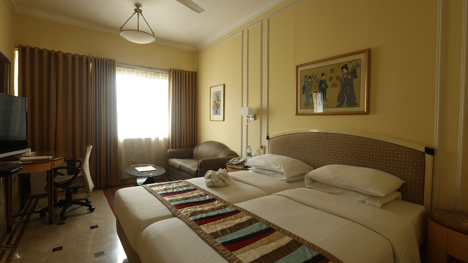 Twin beds in the Superior Room with sunlight peeking through the windows at Regency Hotel, Mumbai.