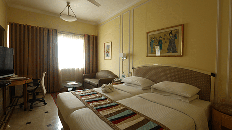 Twin beds in the Superior Room with sunlight peeking through the windows at Regency Hotel, Mumbai.