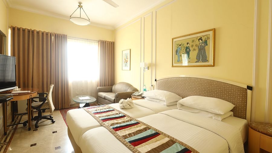 Twin beds in the Superior Room with sunlight peeking through the windows at Regency Hotel, Mumbai.