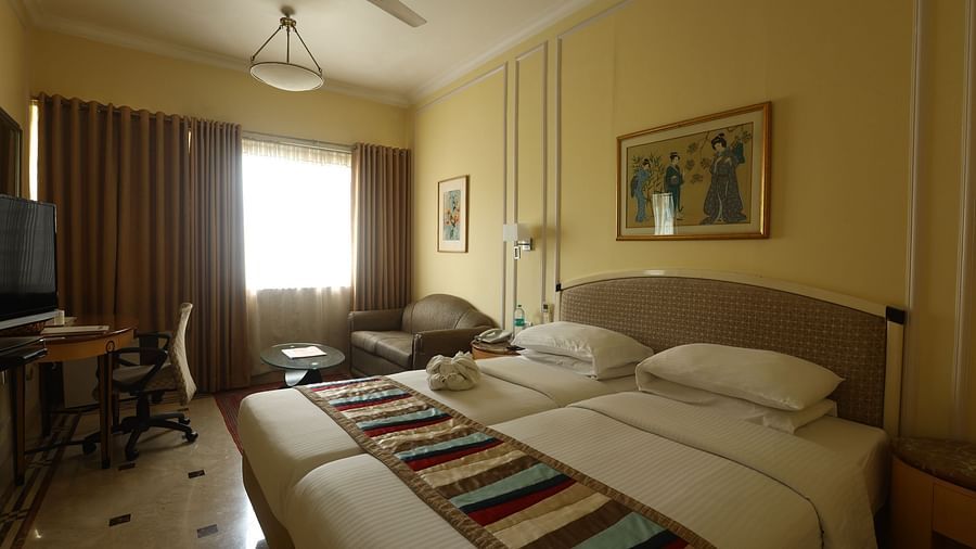 Twin beds in the Superior Room with sunlight peeking through the windows at Regency Hotel, Mumbai.