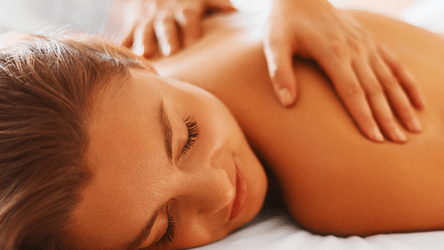 A woman lying on her stomach with her eyes closed receiving massage on their upper back