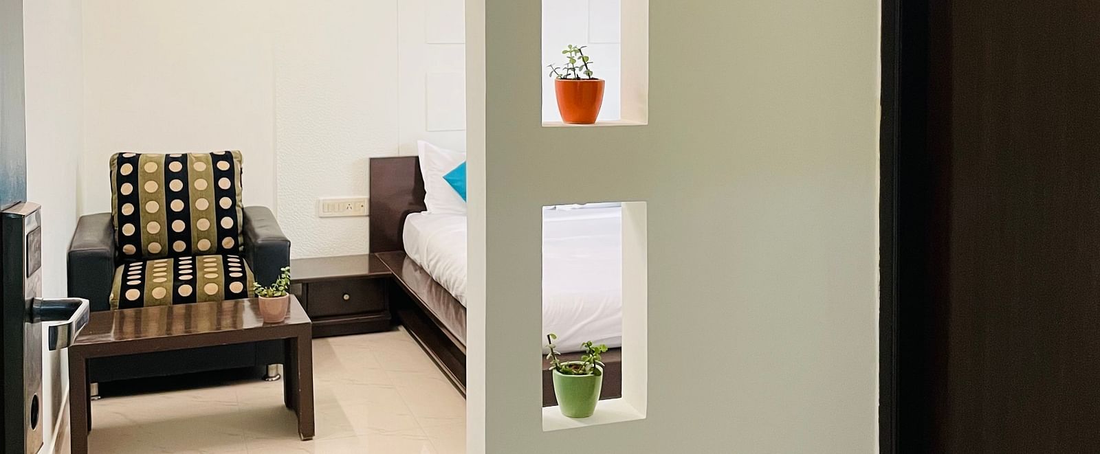 A glimpse into a room with an armchair and a bed beside it at Sanctum Suites Domlur, Bangalore.