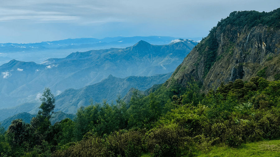 A cliffside view over a misty valley under a cloudy, grey sky.