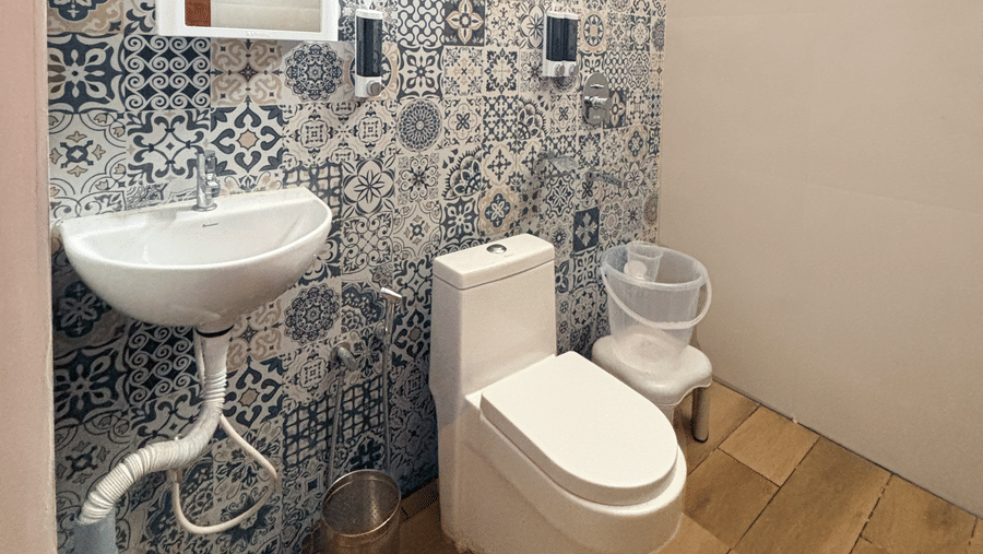 A brightly-lit bathroom featuring a tiled wall along with a commode and a wash basin at WOW Naturefull Resorts, Yercaud.