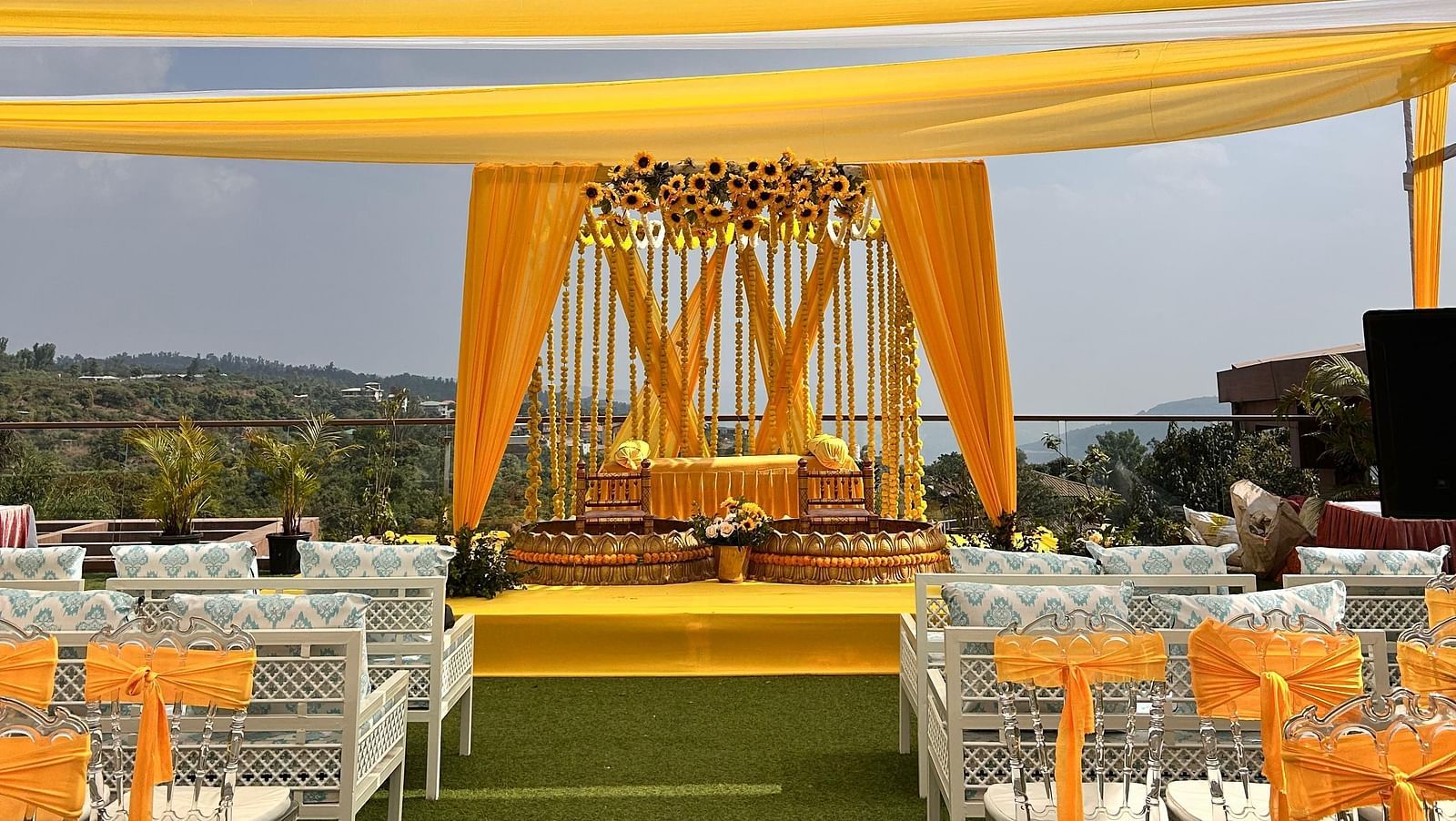 An area decorated with yellow and white fabric pieces, chairs, and a stage decorated with flowers and two seats meant for the bride and groom for their pre wedding rituals at The Grand Legacy Resort & Spa