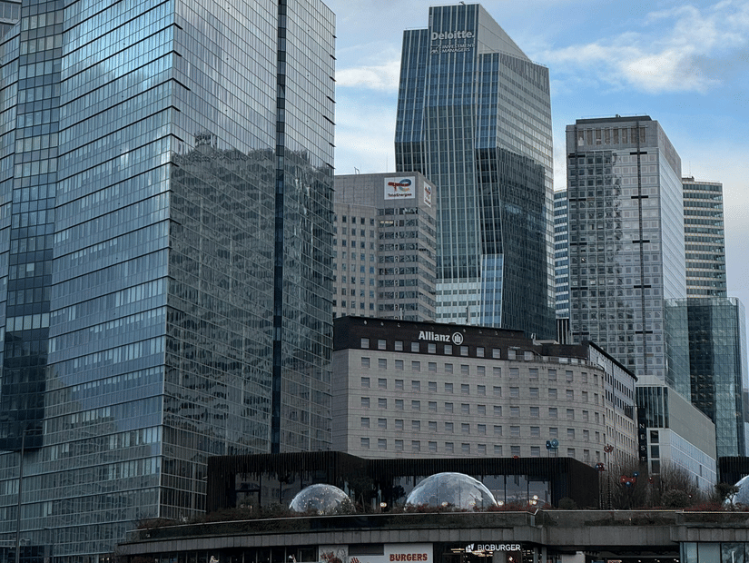 A dense cluster of glass office buildings and skyscrapers under a bright, partially cloudy sky.