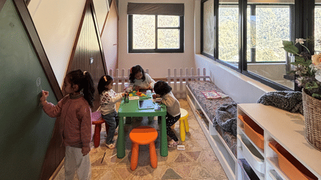 Children's play room with a green chalkboard wall, low table and stools, a cushioned window bench, storage trays and hill windows at The Chamomile Estate.