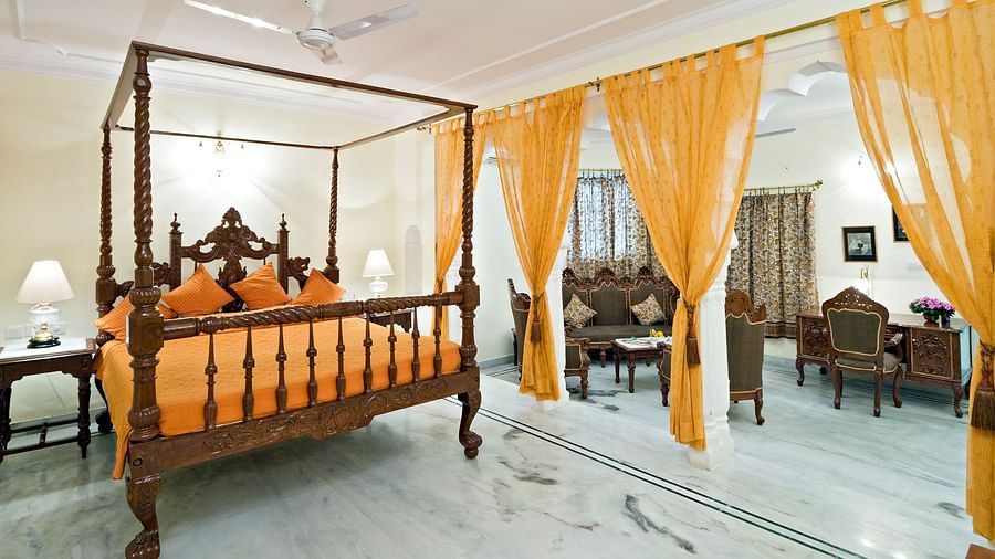 A king bed with lamps on the side tables and sofas in the living room inside the suite - Mandawa Haveli, Jaipur