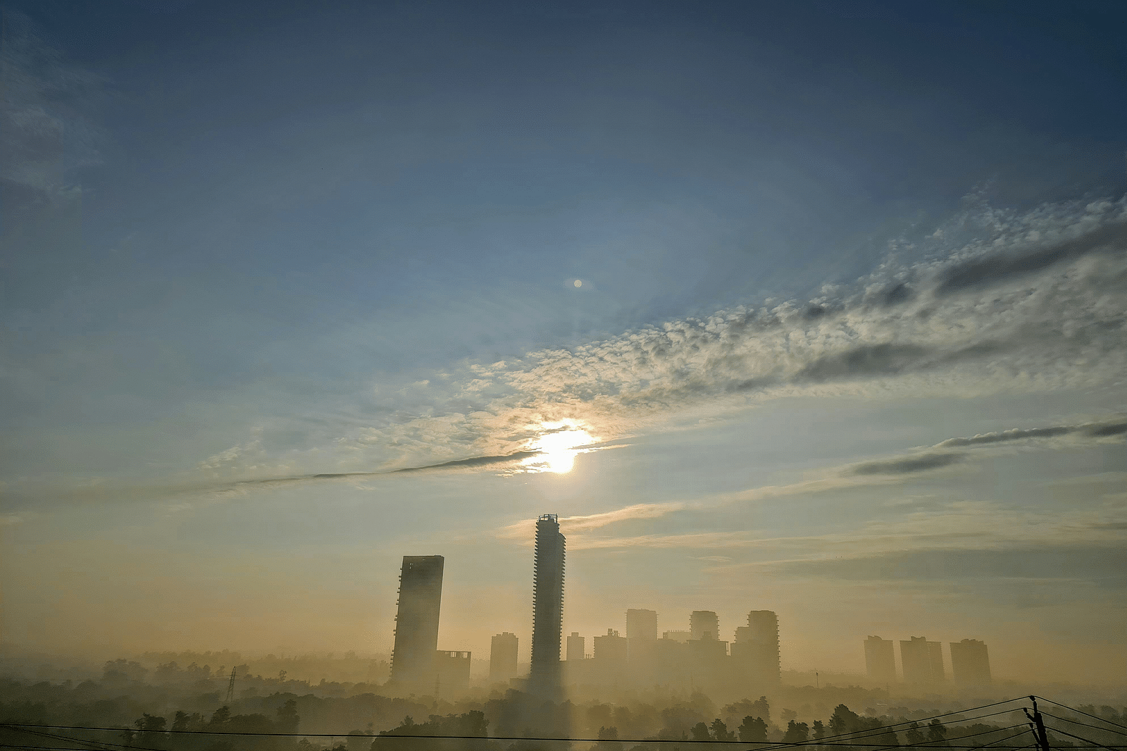 An overview of the city of Gurgaon with the sun just above a high rise building.