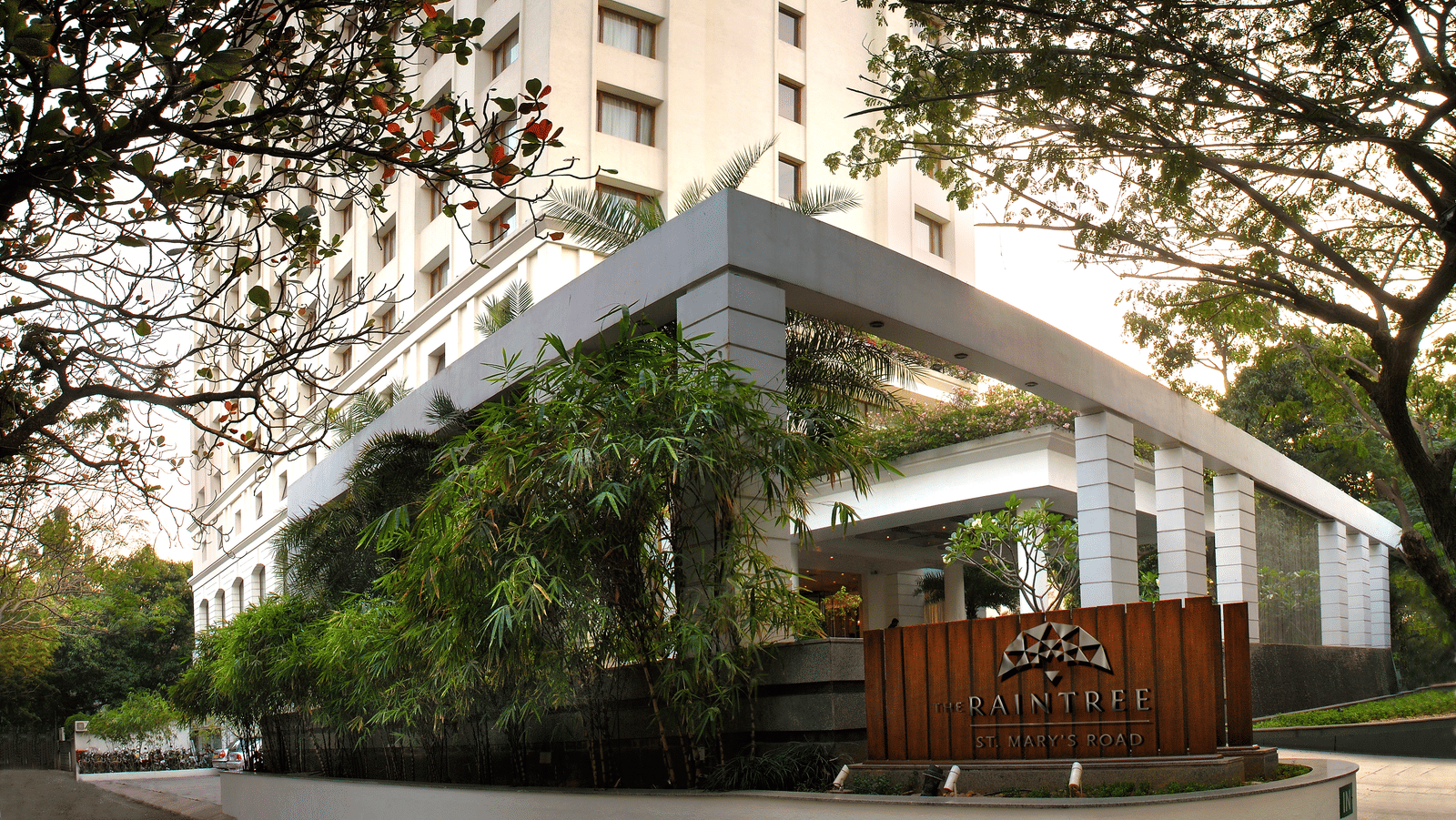 Facade view of The Raintree, St. Mary's Road - Hotel Near Chennai Trade Centre, surrounded by greenery under a vibrant sky