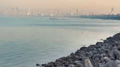 A rocky breakwater extending into the sea with clear waters and a clear sky visible in the background.