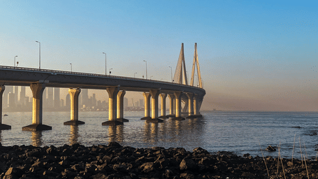 A wide-angle view of the Bandra-Worli Sea Link bridge in Mumbai, stretching across the sea under a clear blue sky at sunrise.