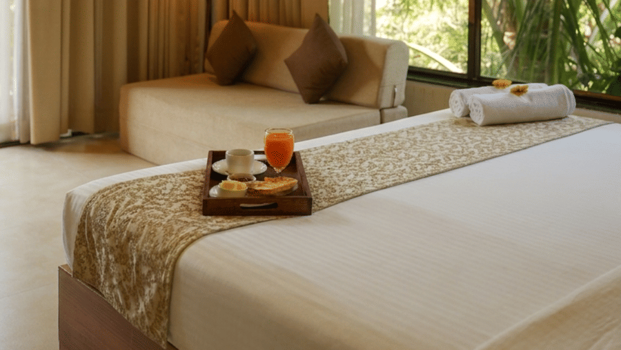 A bedroom at Oceanature Resort, Alibaug featuring a king size bed, a window looking out at trees, and curtains near a sofa.