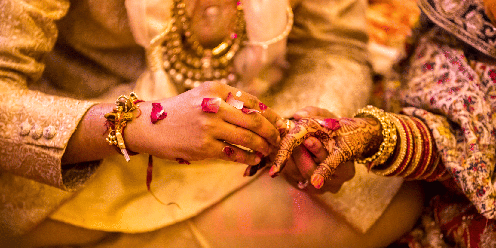 Traditional Indian wedding ceremony with groom placing a ring on bride’s mehndi-adorned hand surrounded by rose petals.