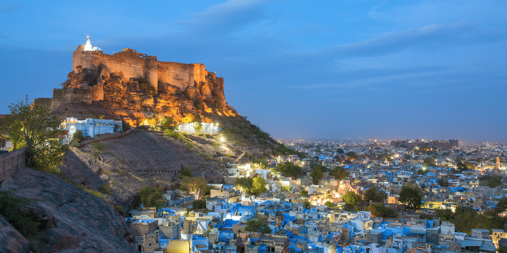 Mehrangarh Fort at dusk dominates the Jodhpur city, where blue-painted buildings glow beneath the hill.