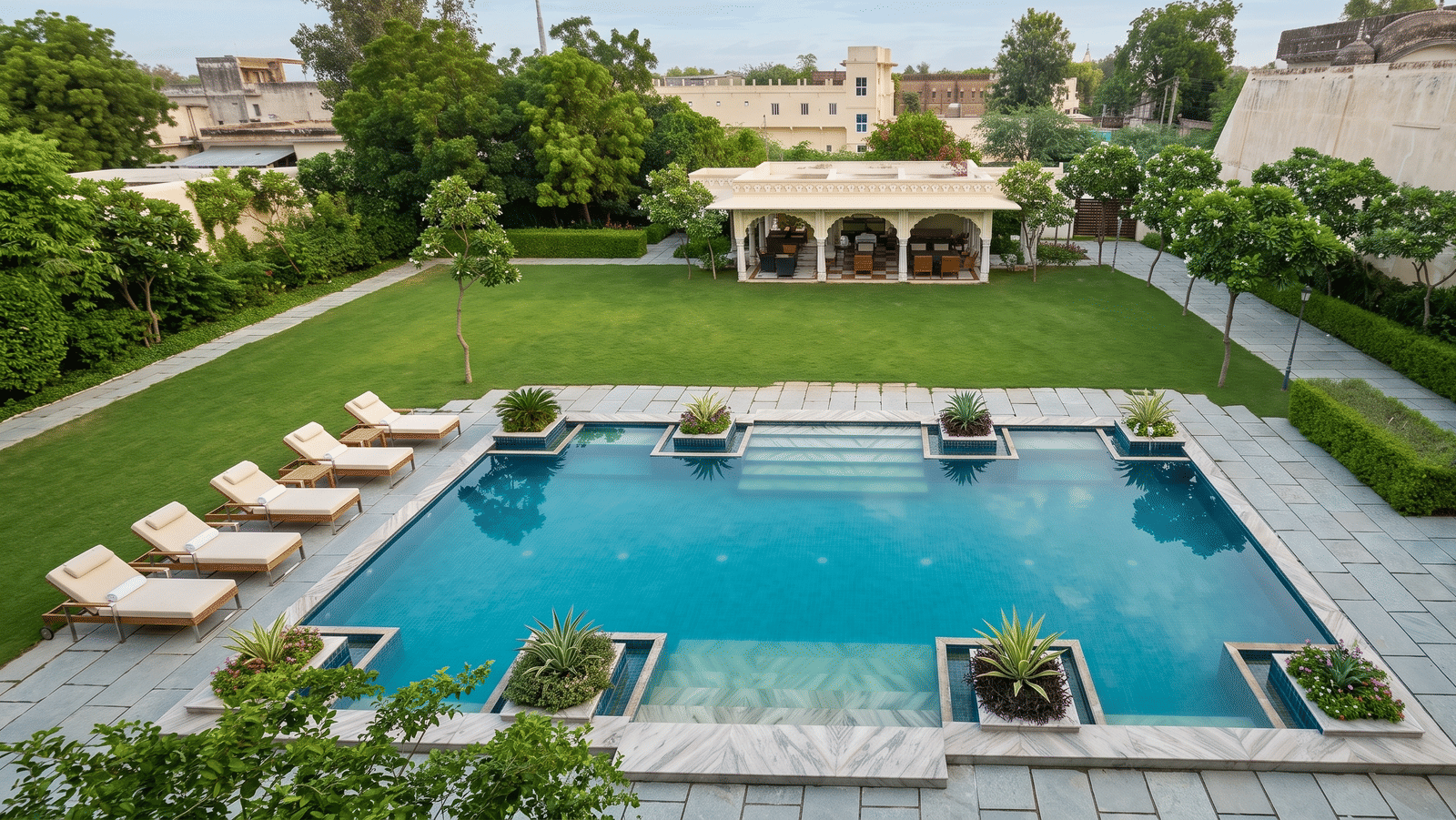 Outdoor swimming pool with sun loungers, planters, a stone-paved deck, lawn and an arched garden pavilion at BluSalzz Vintage - Harlalka Haveli.