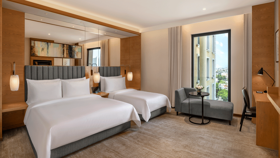 The Suite of Residency Towers, Chennai featuring multiple beds, a wooden flooring, a seating area, a glass window, and overhead lamps.