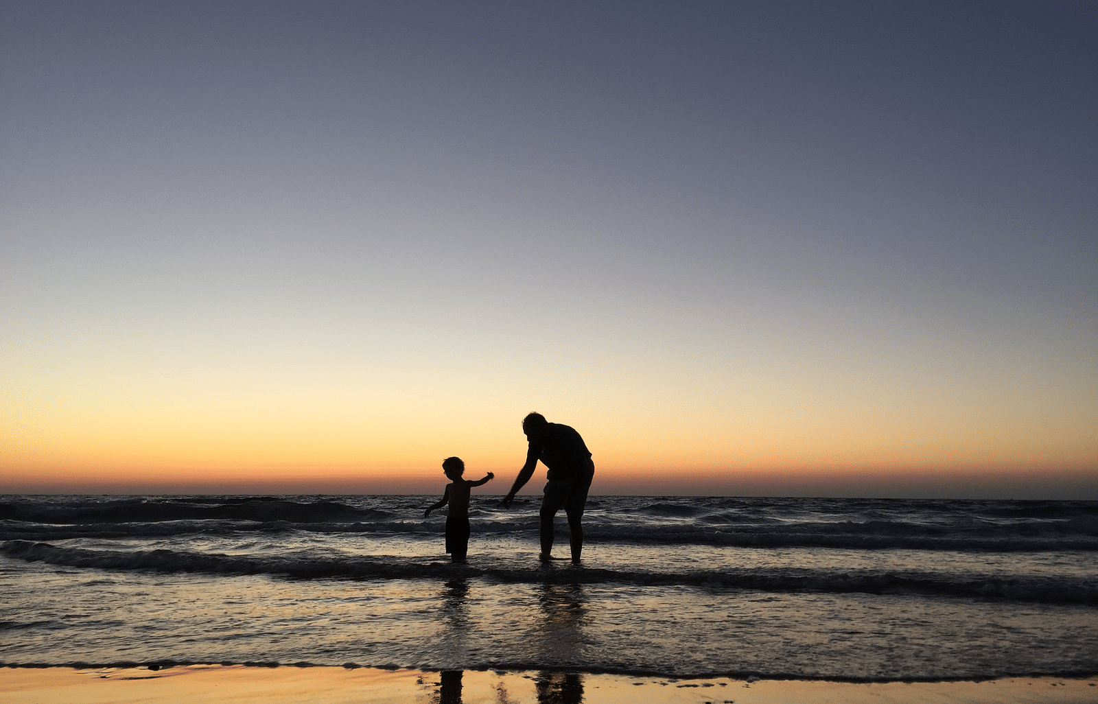Father and child playing on the beach with a peaceful sunset view.