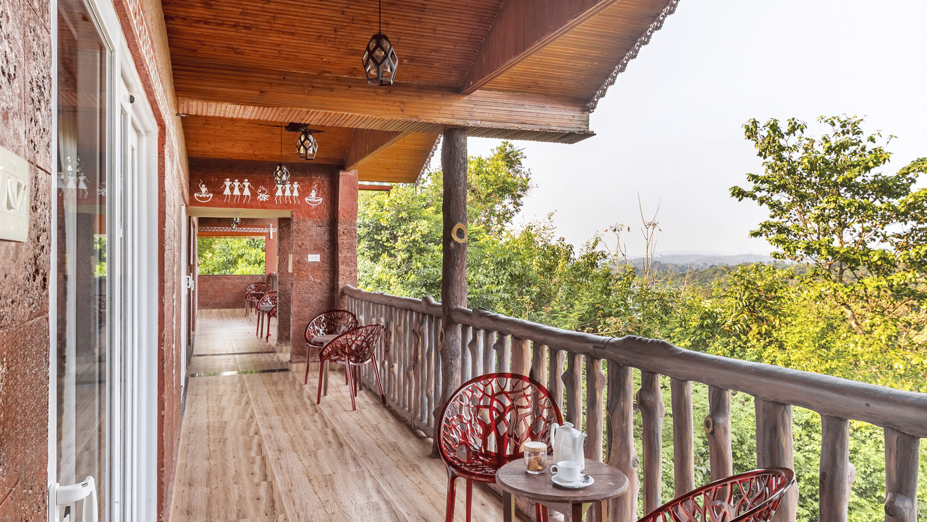 A long balcony with wooden railings and red chairs overlooking the forest.