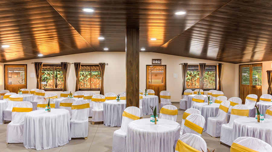 This wide view shows a large hall filled with round tables and white cloths, featuring thick wooden pillars and large windows looking out to the green gardens.
