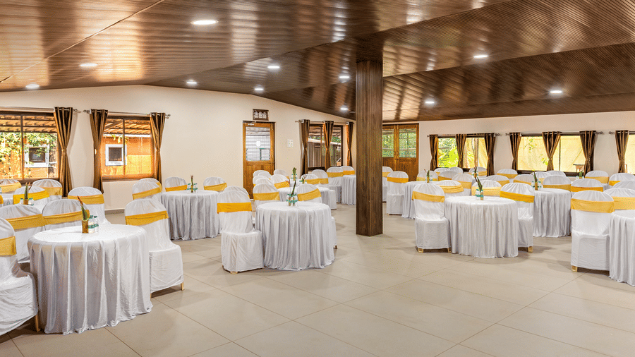 Rows of round tables with white and gold covers fill the large hall, which is supported by stout wooden pillars and illuminated by lights on the wooden ceiling.