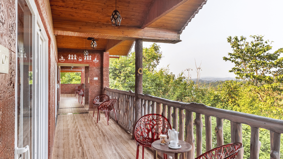 A long balcony with wooden railings and red chairs overlooking the forest.
