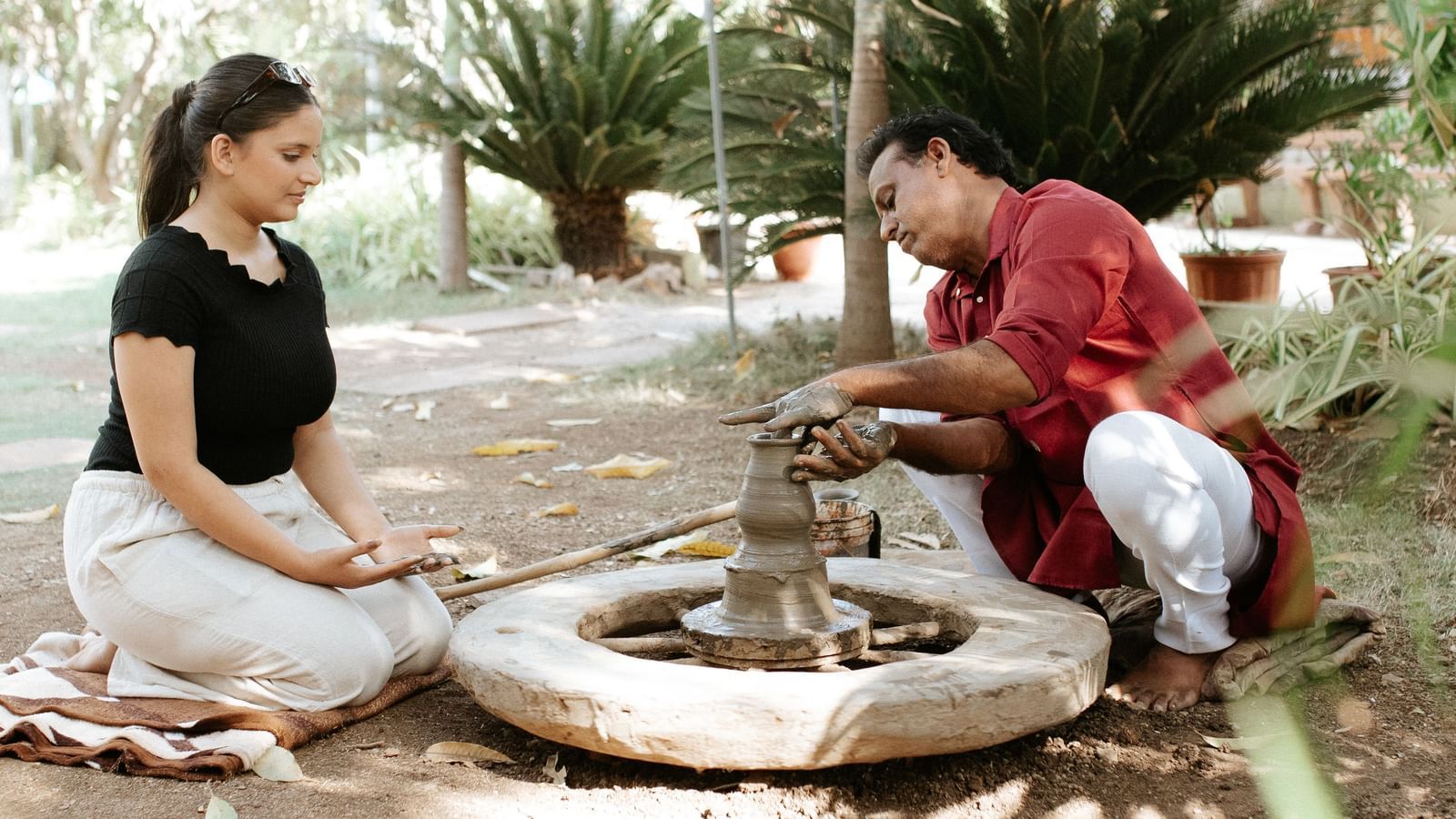 A woman and a man crafting pottery on a spinning wheel outdoors, with greenery in the background at Daksh Resort & Amusement Park.