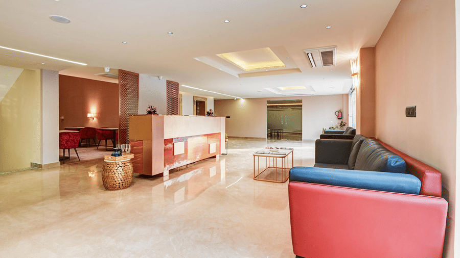 A wide-angle shot of the expansive lobby at Hotel 91 Privé, Gurugram, with a red-coloured couch placed in the waiting area.