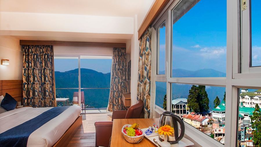 Cosy bedroom with large windows and a balcony overlooking scenic mountains, featuring a welcome tray with fruits and tea essentials - Central Heritage Resort and Spa