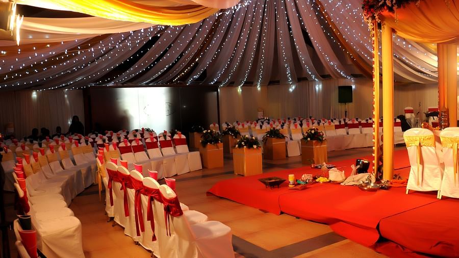 An image of a beautifully decorated wedding venue with chairs arranged, a decorated stage at the front, and shimmering lights hanging from the ceiling