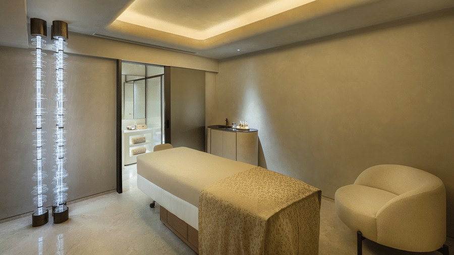 Therapy room at Aavraa Wellness of The Residency Towers Chennai featuring a massage bed with a couch next to it and a table next to the way to the washroom