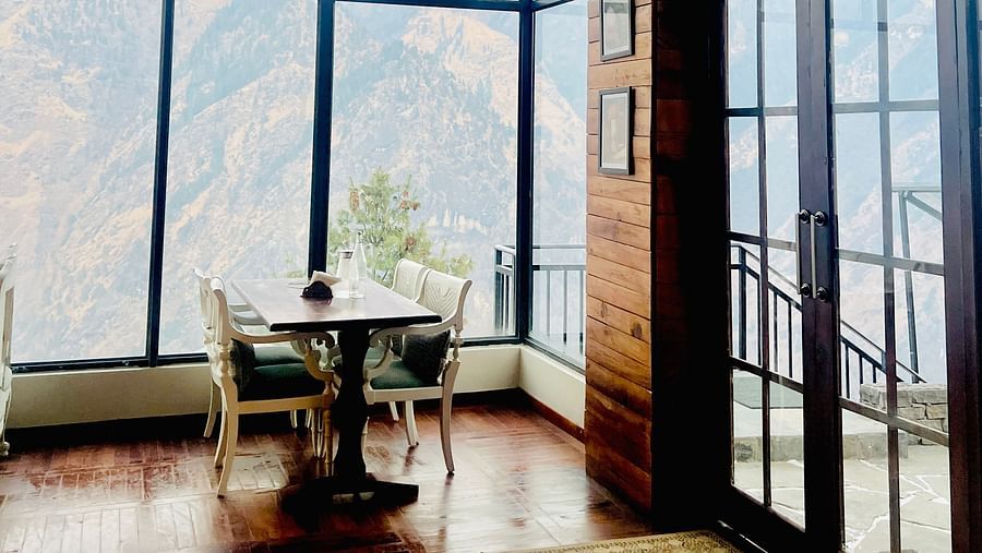 Image of a dining space with table and chairs and large windows overlooking the mountinas | Faraway Cottages, Auli