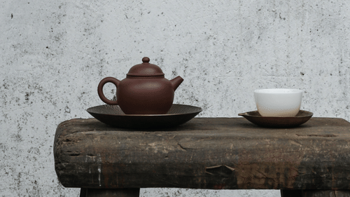 A Chinese teapot with a cup next to it on a wooden chair