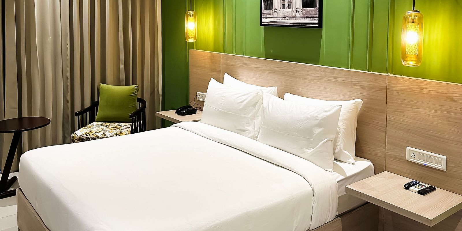 A hotel room with a large comfortable bed, wall lamps attached near the head bed and a painting on a green wall - Wonder Hills