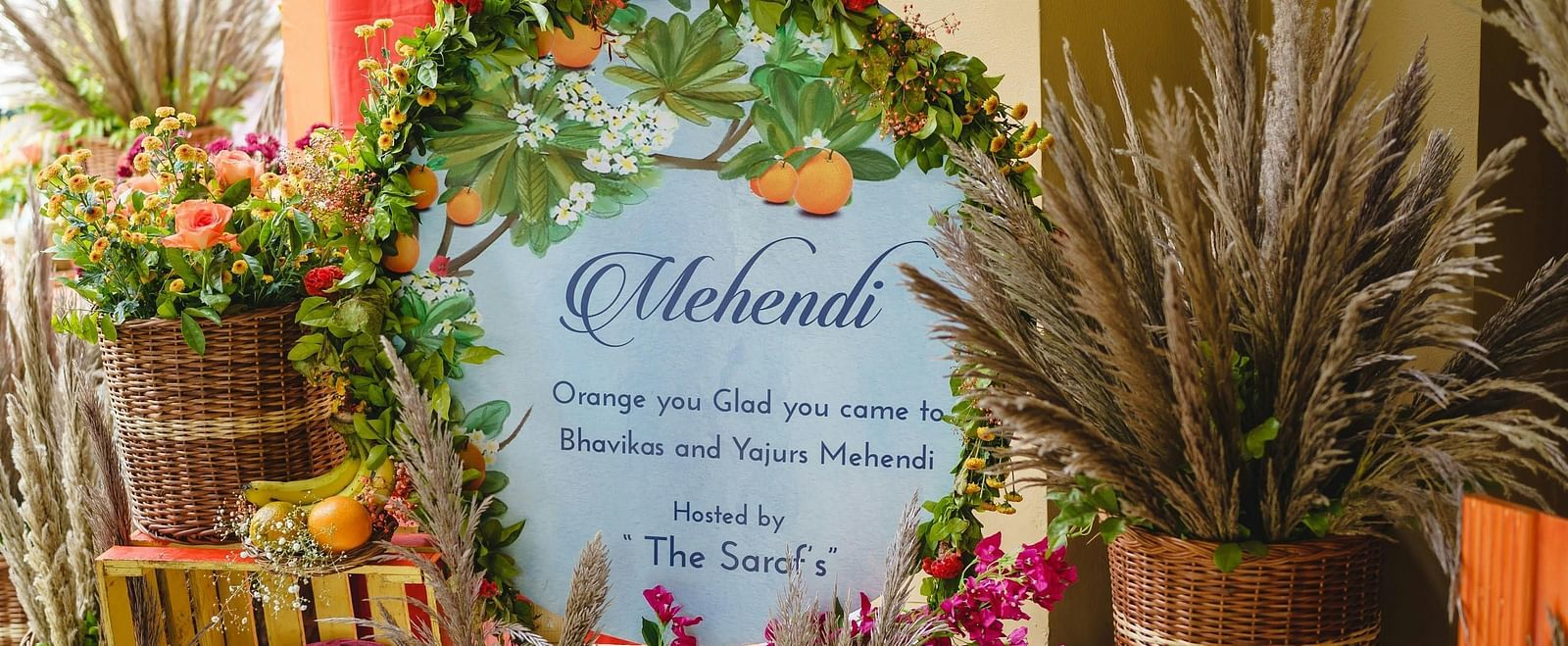 A close up of a board surrounded by fruits and flowers welcoming the guests to a wedding function.