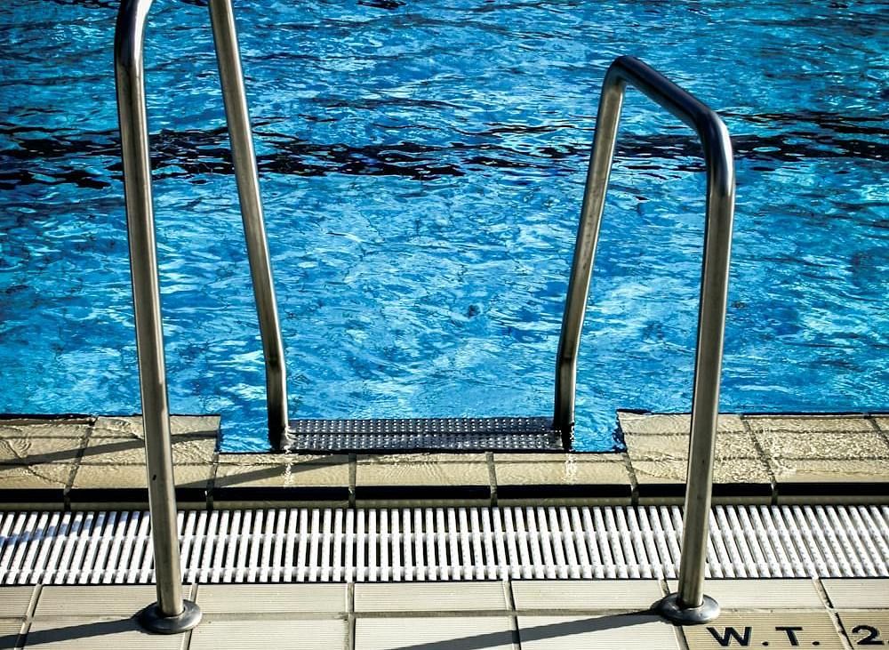 An image of a swimming pool ladder and swimming pool in the background.