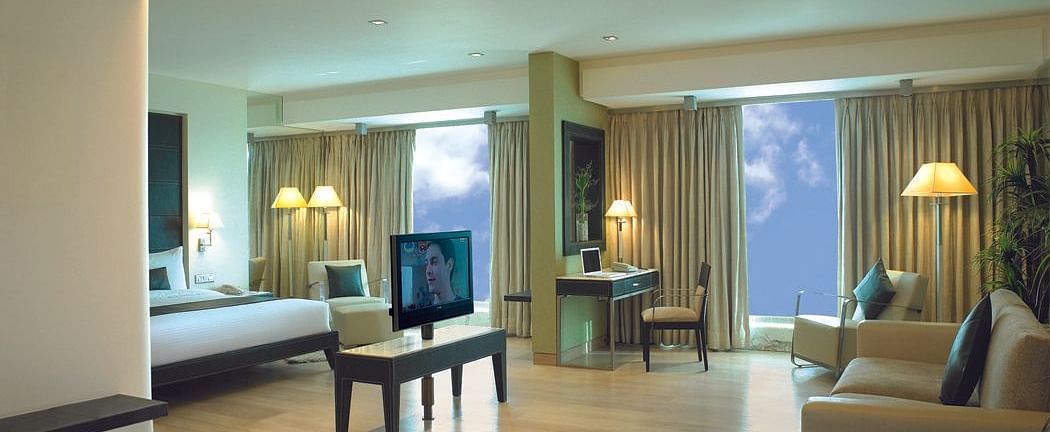 Shot of the expansive suite at our hotel featuring a separate living area, sofa, side lamp, a television, and a king size bed. | Mirage Hotel