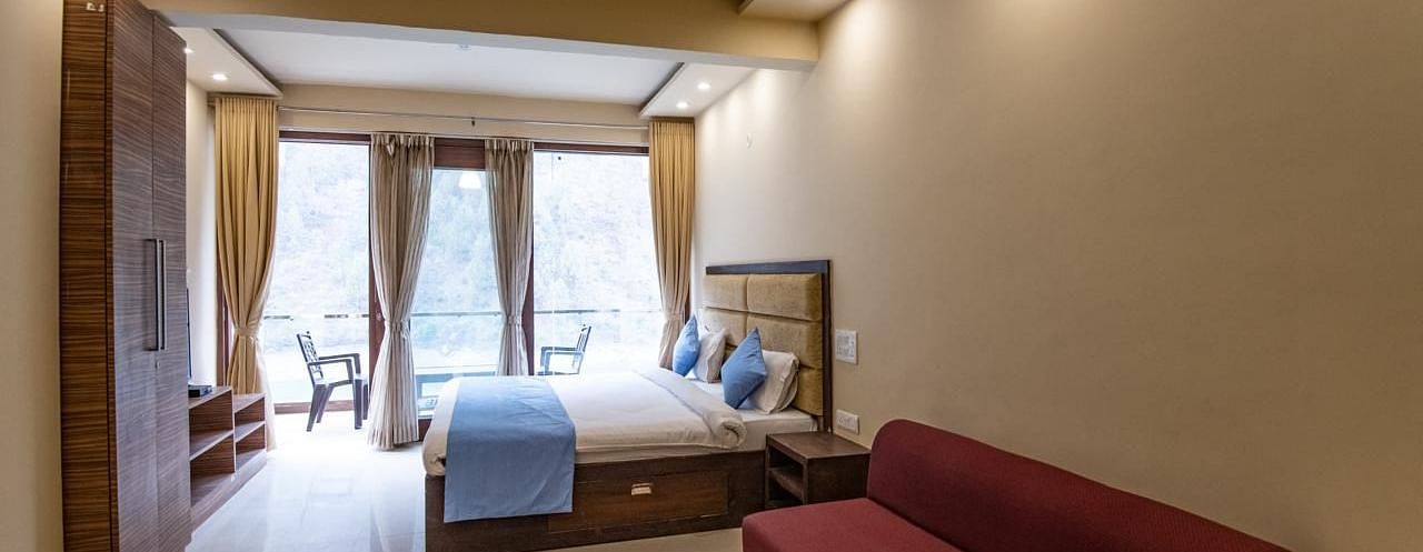 Spacious room featuring a bed, wall-mounted TV, sofa, and balcony view through glass doors.