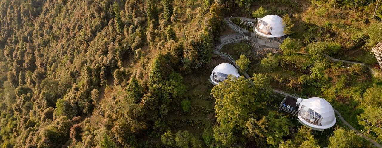 An image of three dome style separate bedroom and a pathway leading to one another amidst a lush garden