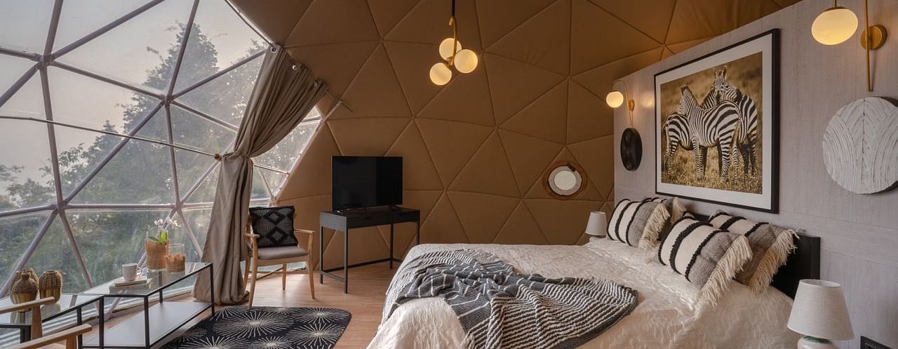 An image of a bedroom in dome cottage with king size bed, bedside table, flat TV screen, chandeliers, etc. | Avalon Cottages, Kanatal