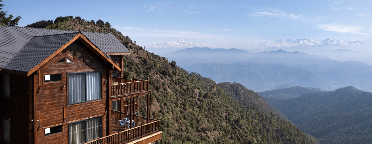 A view of a cottage and the balcony with a backdrop of mountains and clouds | Avalon Cottages, Kanatal