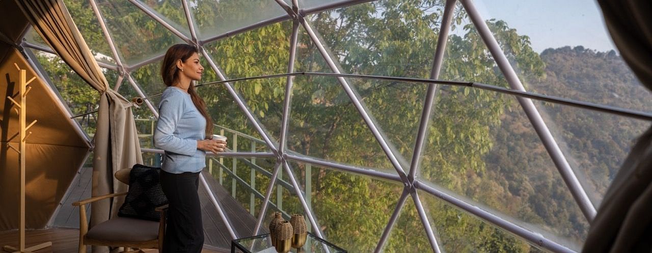 An image of woman enjoying the view from a dome cottage | Avalon Cottages, Kanatal