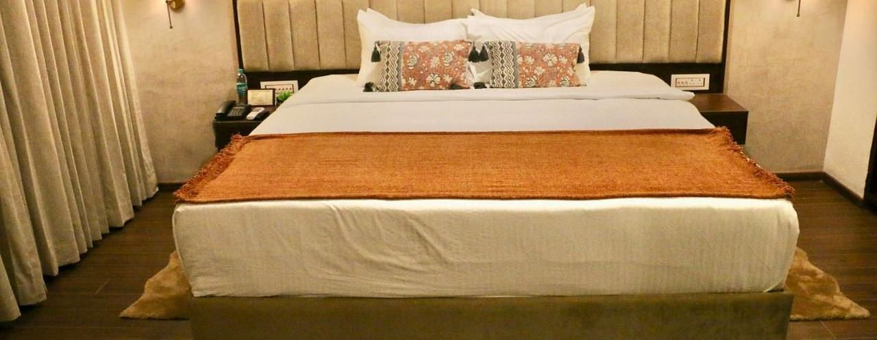 A neatly made bed with white and orange linens of Luxury Junior Suite at Nalapad Hotel Bangalore International.