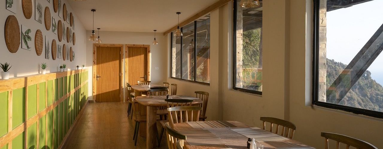 An image of a dining area with several chairs and table placed at one side with widows| Avalon Cottages, Kanatal