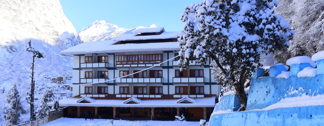 Image of the hotel covered with snow with mountains on either side and few trees   | Yashshree Lachung