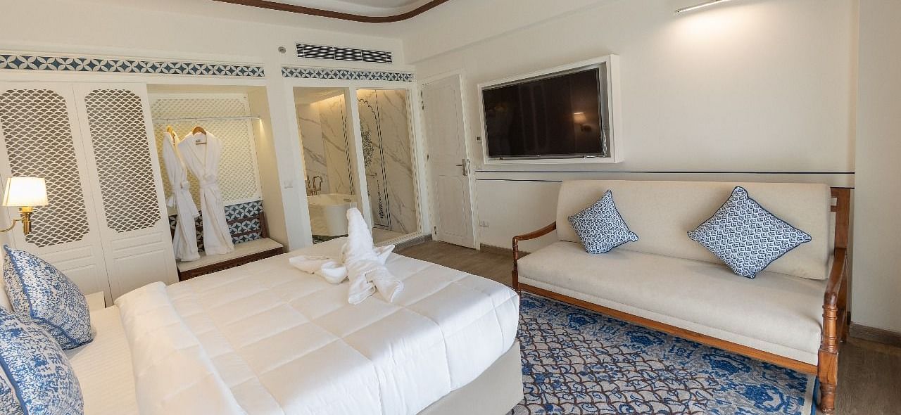 Corner view shot of the bedroom at Ananata Room featuring a plush double bed alon with a television and a couch in front of it at Bhagirathi by RDB Atishay.