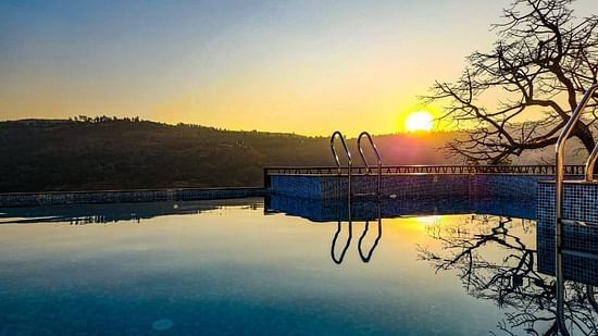 The outdoor swimming pool at VITS Panchgani with the sun setting behind the mountains in the backdrop
