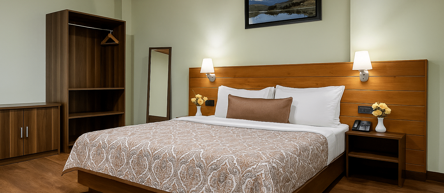 A neatly arranged hotel room at Summit Enigma Resort & Spa features a large bed with a patterned duvet, a wooden headboard, bedside tables with lamps, an open wardrobe, and a framed landscape picture above the bed.